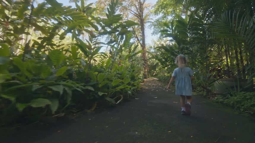 Little girl plays as she walks on a path through a tropical garden in the forest