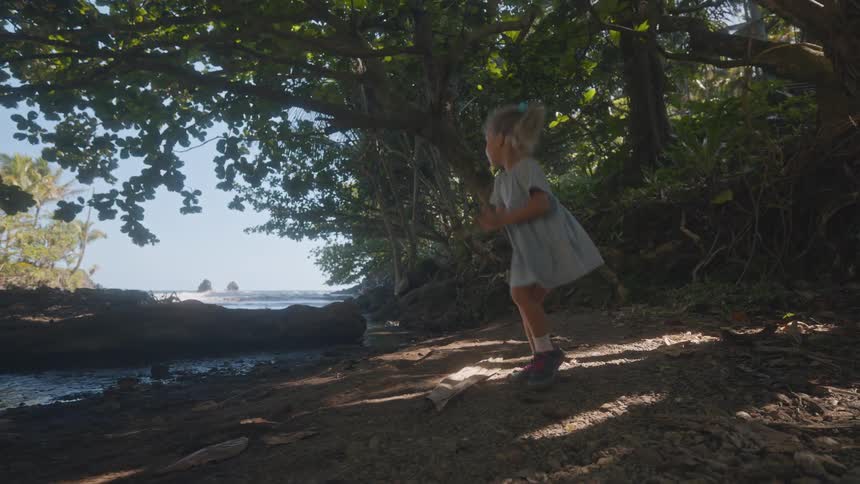 Little girl walks along the coast under trees as she throws a rock into the water