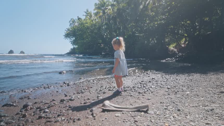 A childplaying on a beach filled with small rocks as she runs away from the waves excitedly