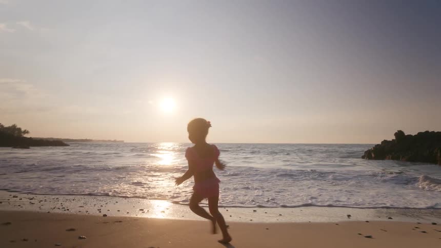 Child running on sand at sunset with golden silhouette and sea reflecting soft light