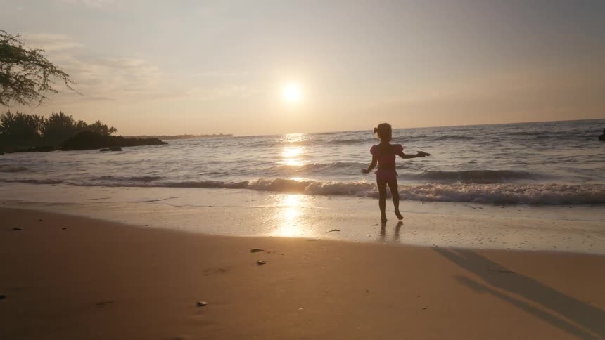 The girl runs on the beach and dumps sand in the ocean