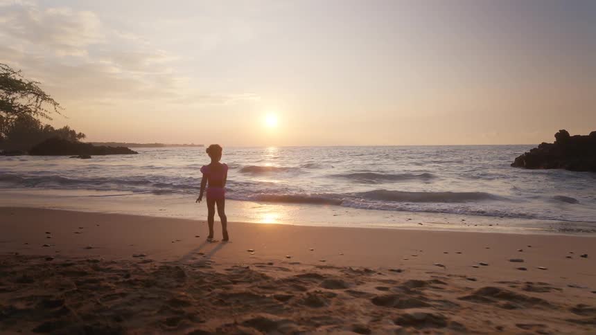 A child playing excitedly in the beach sand at sunset the warm light glowing across the shoreline
