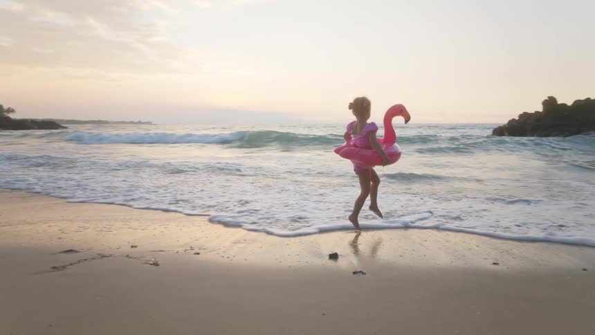 A young girl wearing a duckshaped pool float running across the beach sand at midday and having fun under the bright sun