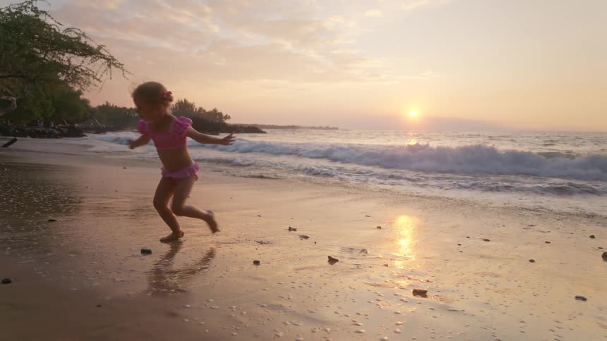 Child running on beach at sunset with golden reflections on water and colorful sky
