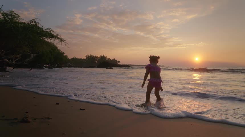 Child walks on wet sand during sunset