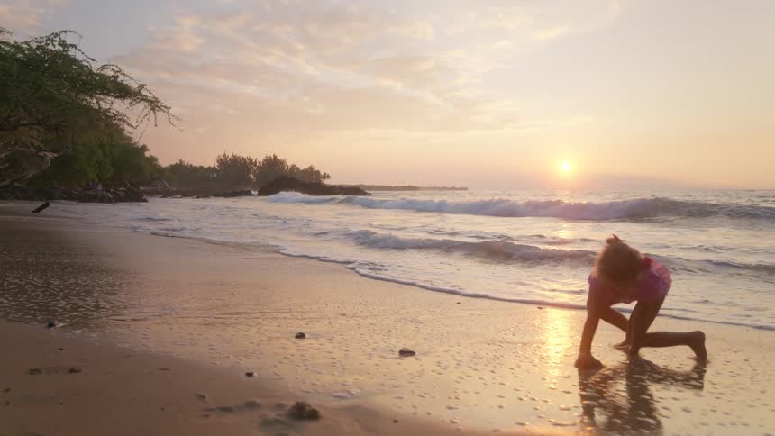 Child walking along beach at sunset with golden silhouette and reflection on wet sand