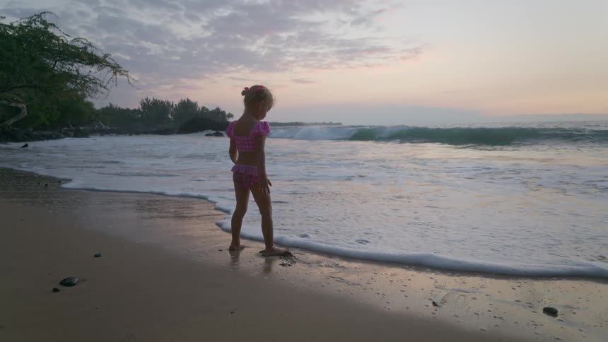 Little girl playing on the beach walking in the water as waves roll in to shore
