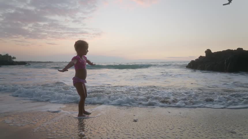 Kid watches the sea with feet in the water at dusk