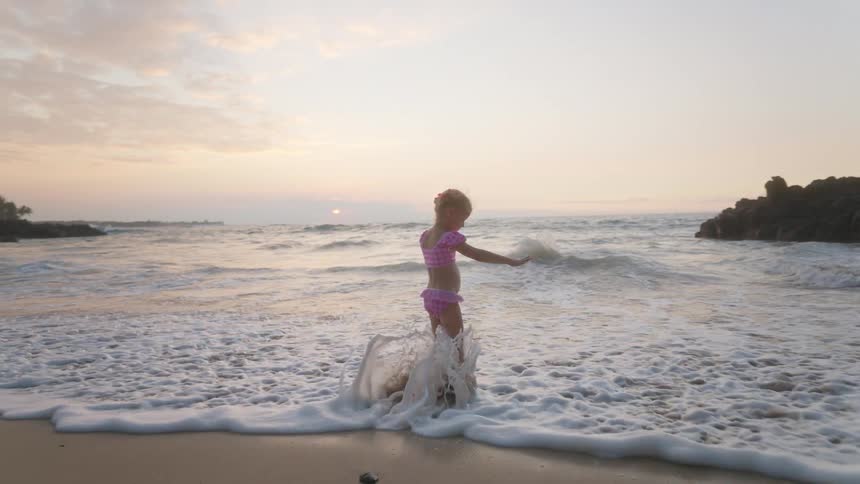 Child in pink swimsuit playing at oceans edge during sunrise