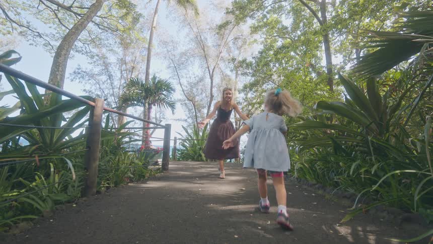 Mother and daughter walk hand in hand along a treelined path