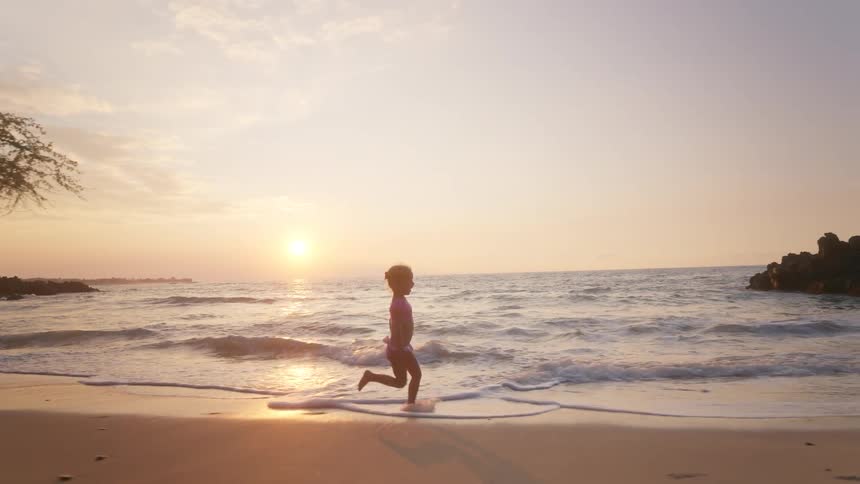 Little girl running across the beach as waves roll in to shore
