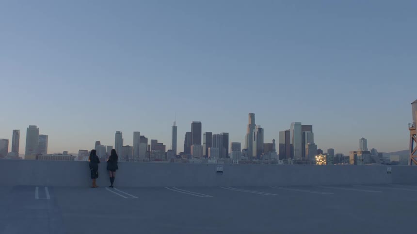 Two young woman standing on the top floor of a parking garage with a view of the metropolitan skyline in the distance
