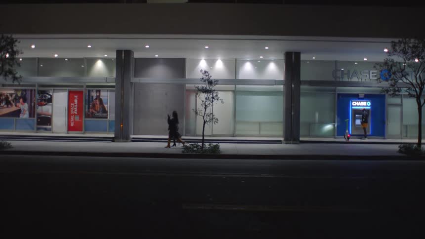 Person walks on lit sidewalk in front of modern bank branch