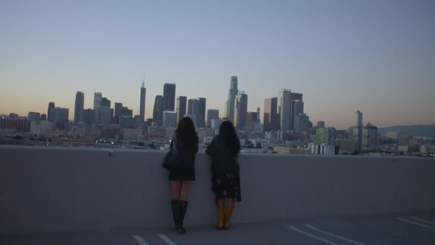 Two women look at the large city from the rooftop