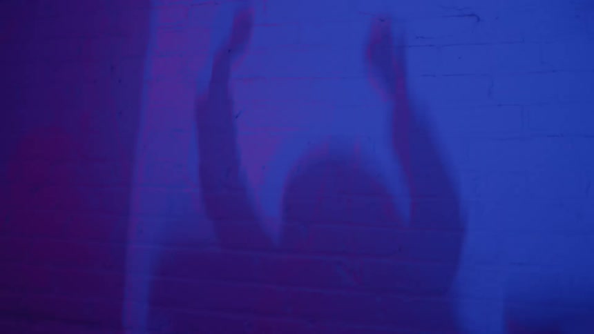 Silhouette of a person dancing with raised arms under purple and blue lighting