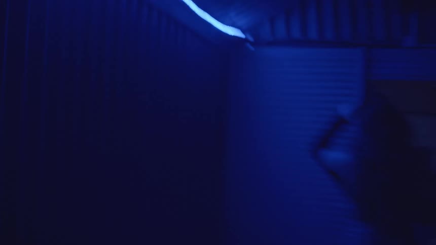 Night club attendees walk through an area dimly illuminated by blue lighting