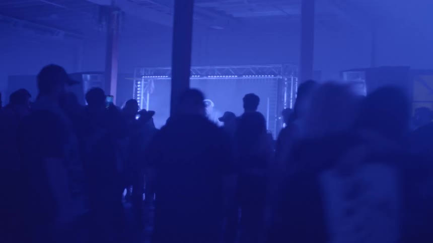 People gathered in a nightclub with blue lighting and a stage in the background