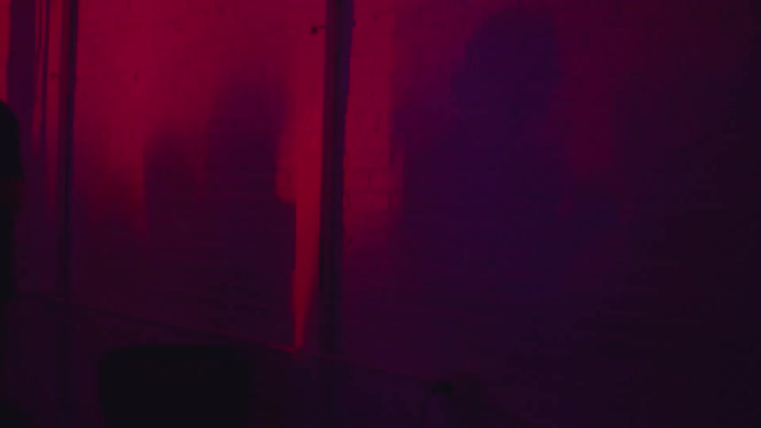 Blue and red lights pulse rhythmically casting fluid moving shadows of dancing people across a dark wall