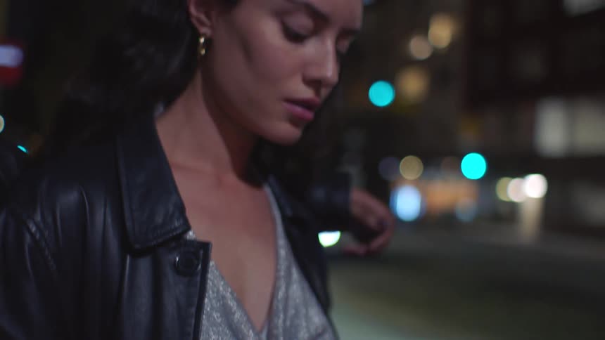 Hands holding a smartphone in a nighttime urban setting with blurred lights in the background