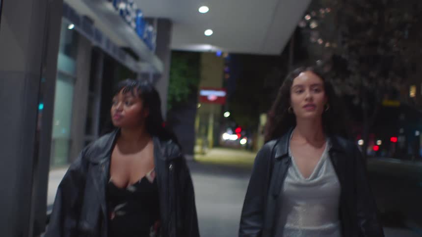 The two women walk past the buildings at night