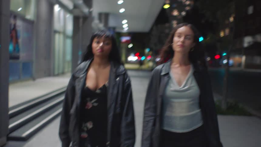 Women walking on a lit urban sidewalk at night