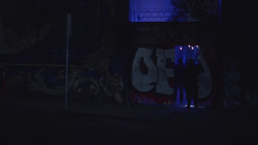 People entering a nighttime venue illuminated by blue light in an urban area