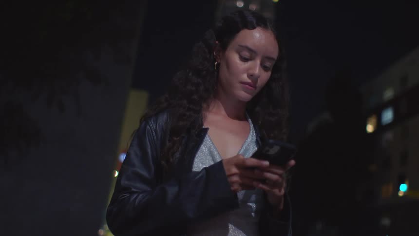 A woman texting on a phone outdoors at night