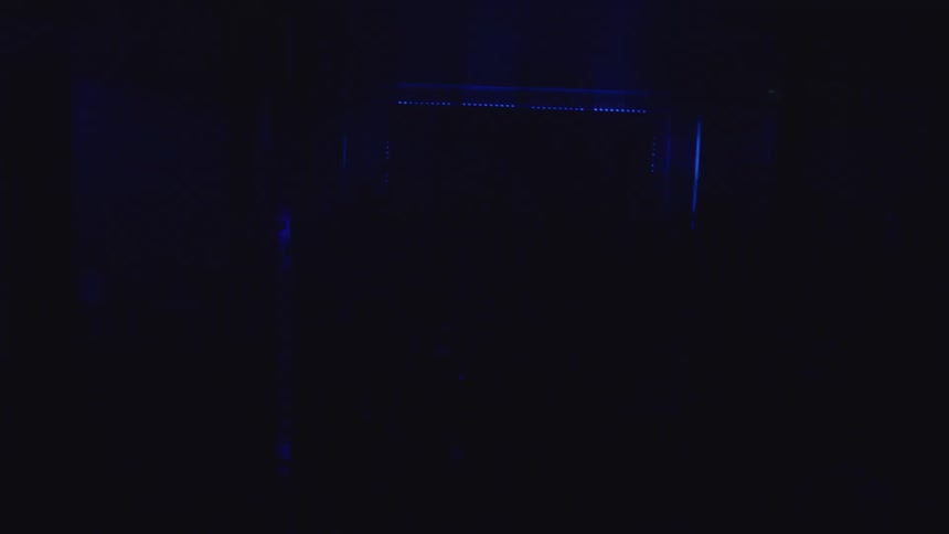 A nightclub filled with people dancing in a dark room the atmosphere pulsing as a blue light flickers across the crowd