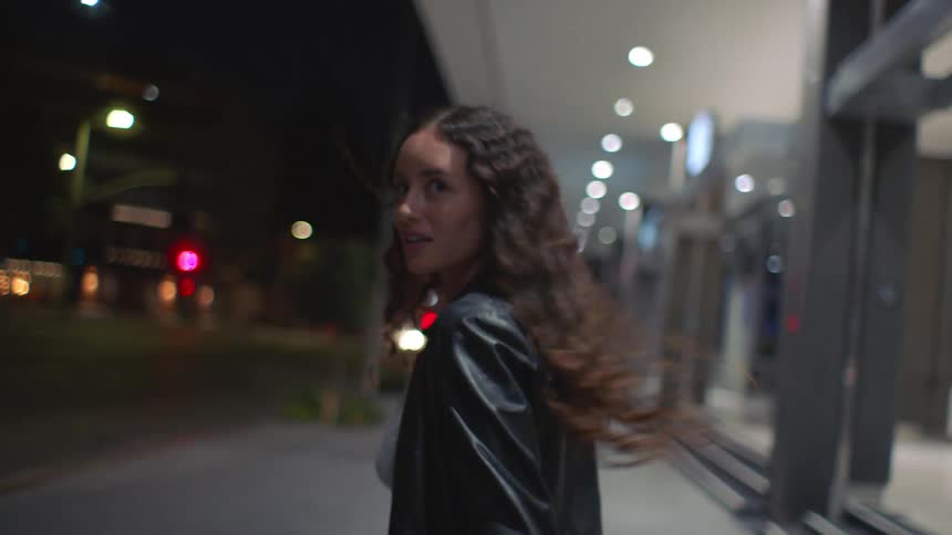 Two people running hand in hand along an urban sidewalk at night with blurred city lights in the background