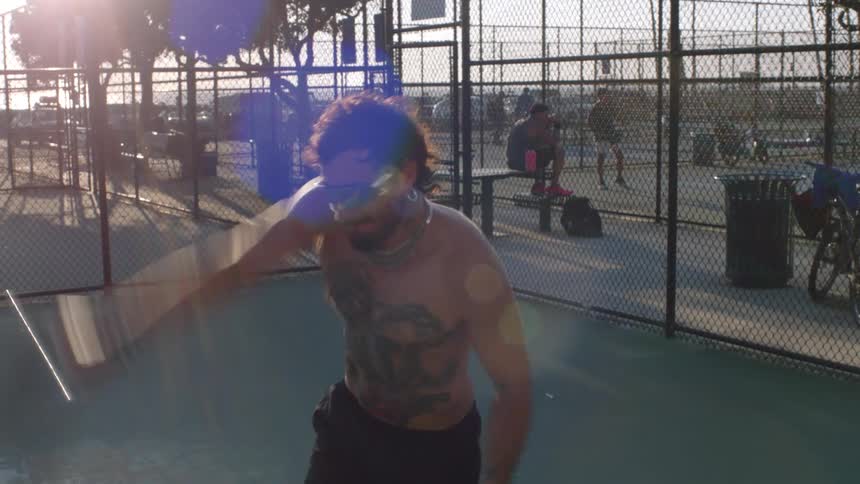 Shirtless man practicing a racket sport on an outdoor fenced court