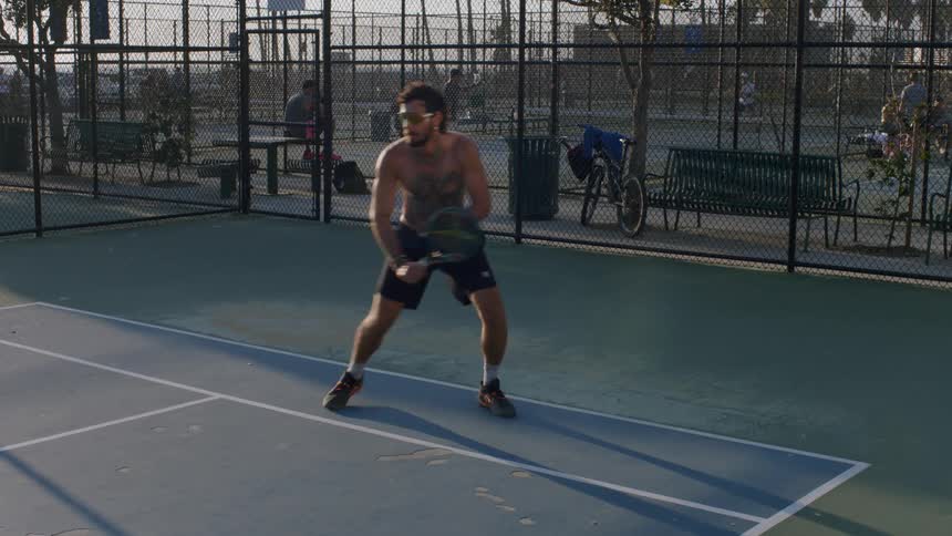 Shirtless man playing tennis on an outdoor court