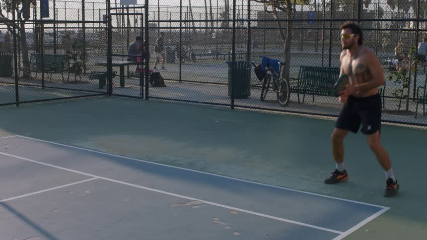 Man hits the ball with a swing between his legs during a summer tennis game