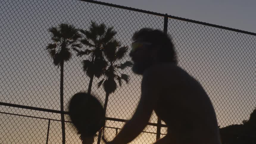 Bare chested man plays tennis after dusk during the summer