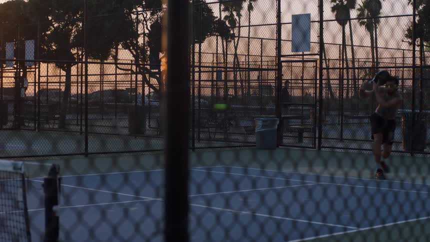Player runs toward the ball during a match on a fenced outdoor sports court