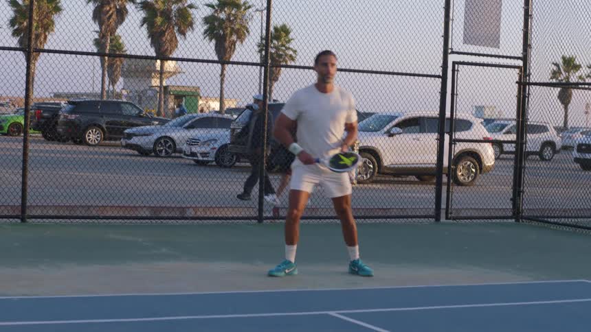 Man playing tennis on a court at dusk