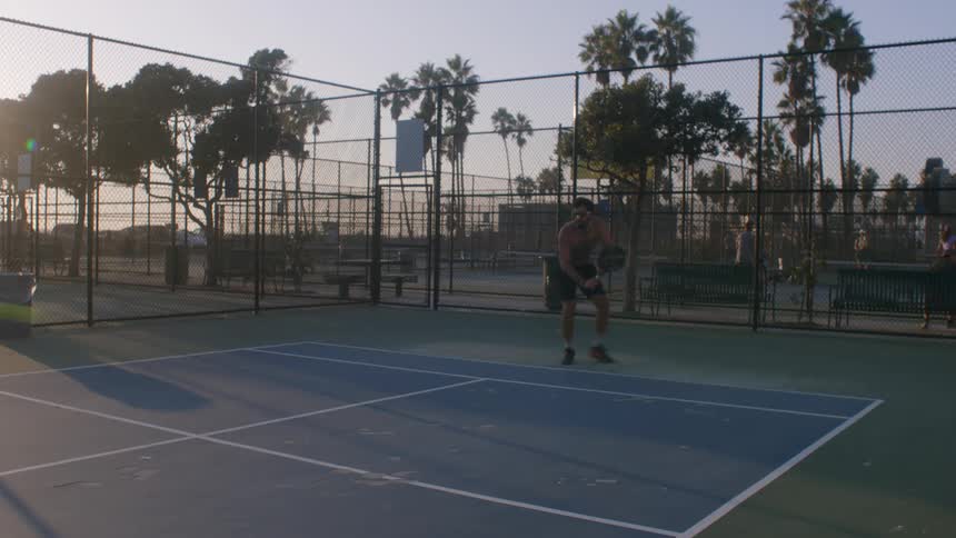 Player positions himself at the back of the court while tracking the ball on a fenced outdoor sports court