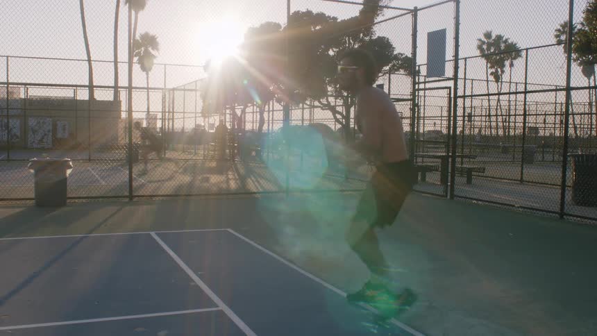 Player jumps and hits the ball with a racket on a fenced outdoor sports court at sunset