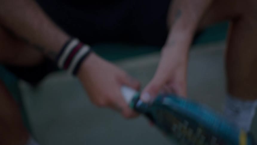 Hand holds a sports racket with a white grip over the court surface