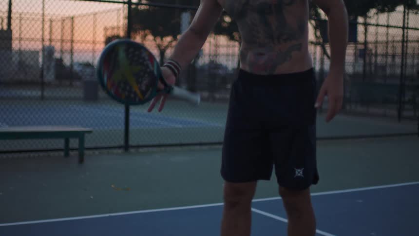 Man spins a sports racket while on an outdoor court at dusk