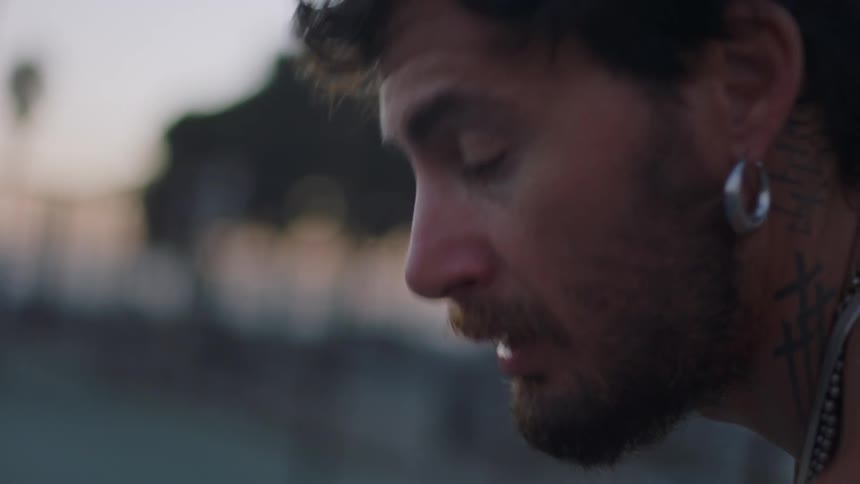 A man with a beard hoop earring and neck tattoo is concentrating looking to the side
