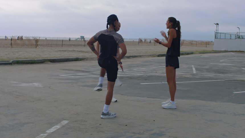 Two young men stretching outdoors at midday while a woman beside them talks
