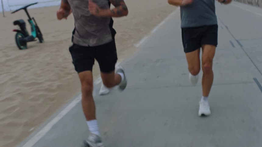 A group of four people running on an asphalt path alongside the sand of a beach