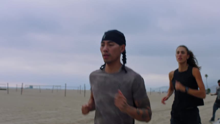Man followed by a woman running along the beach on a cloudy day