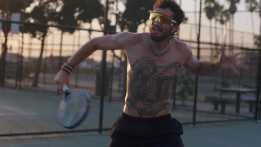 A shirtless man is hitting a small ball with a racket on a court