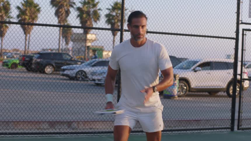Man playing tennis on a court at dusk
