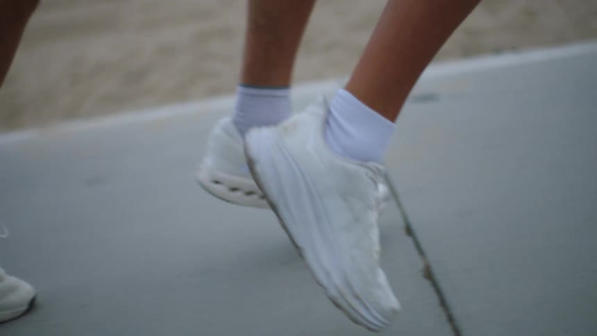 Two people wearing white sneakers running on a paved area