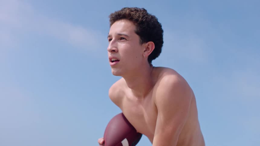 Shirtless man outdoors holding an american football