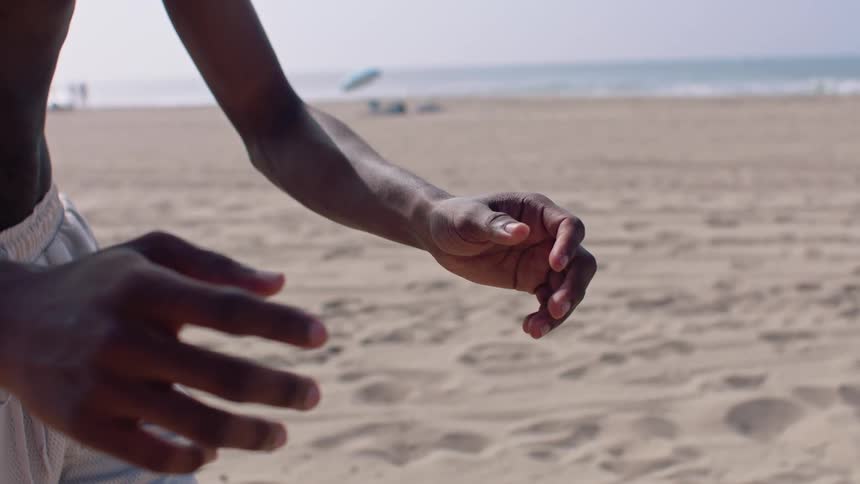 Closeup of a mans hands mid motion on a sandy beach with the ocean behind