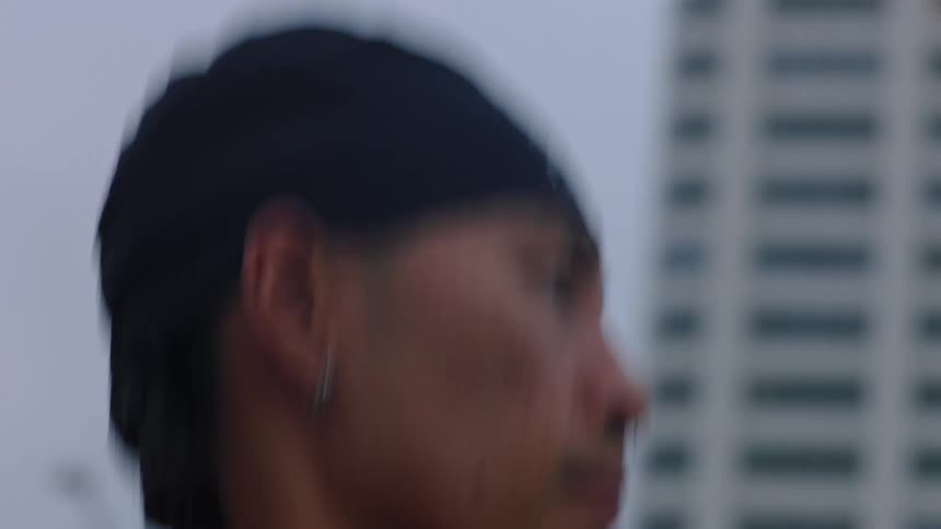 A young man with braided hair jogging down a city street at midday