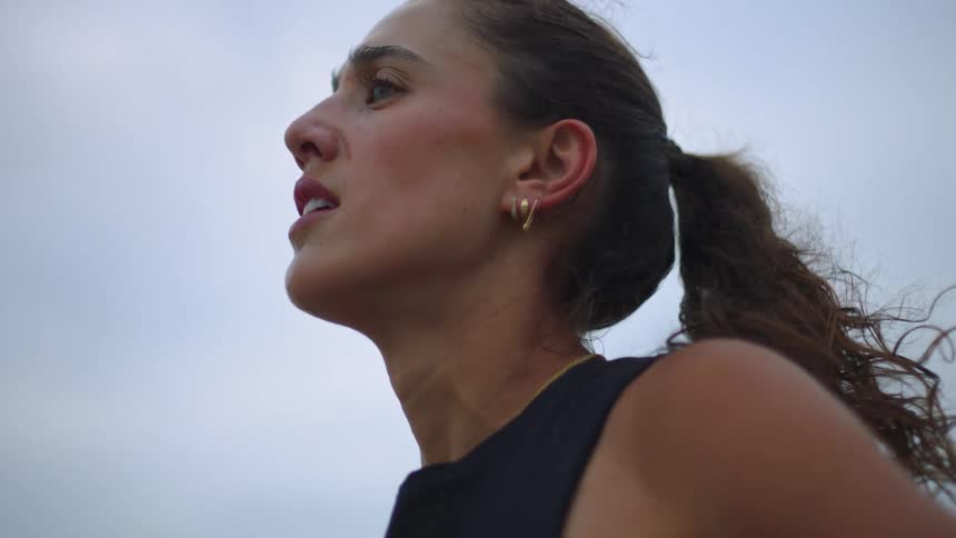 An athletic woman pauses to catch her breath her determined face tilted toward the overcast sky as she takes a deep restorative breath and stretches